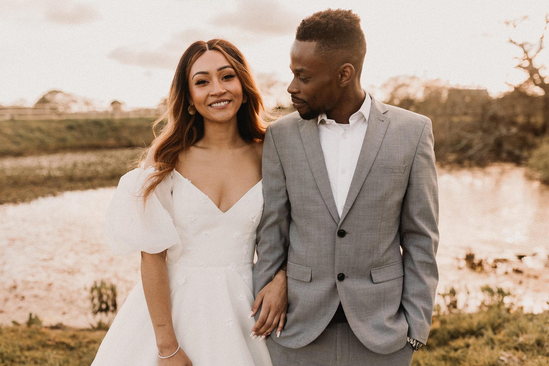 Newlyweds walking through tall grass at sunset