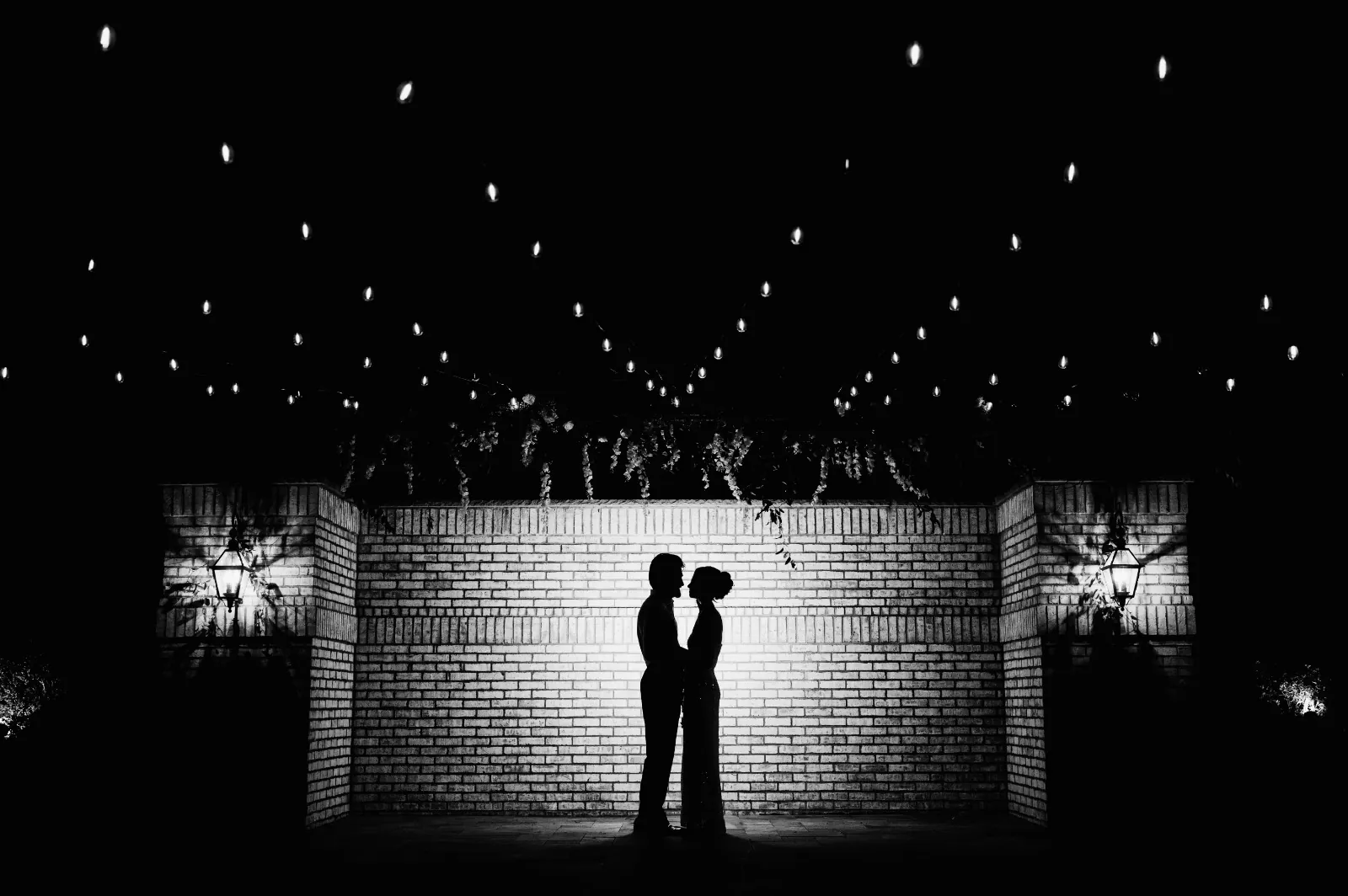 A couple silhouetted beneath strings of light at an evening reception