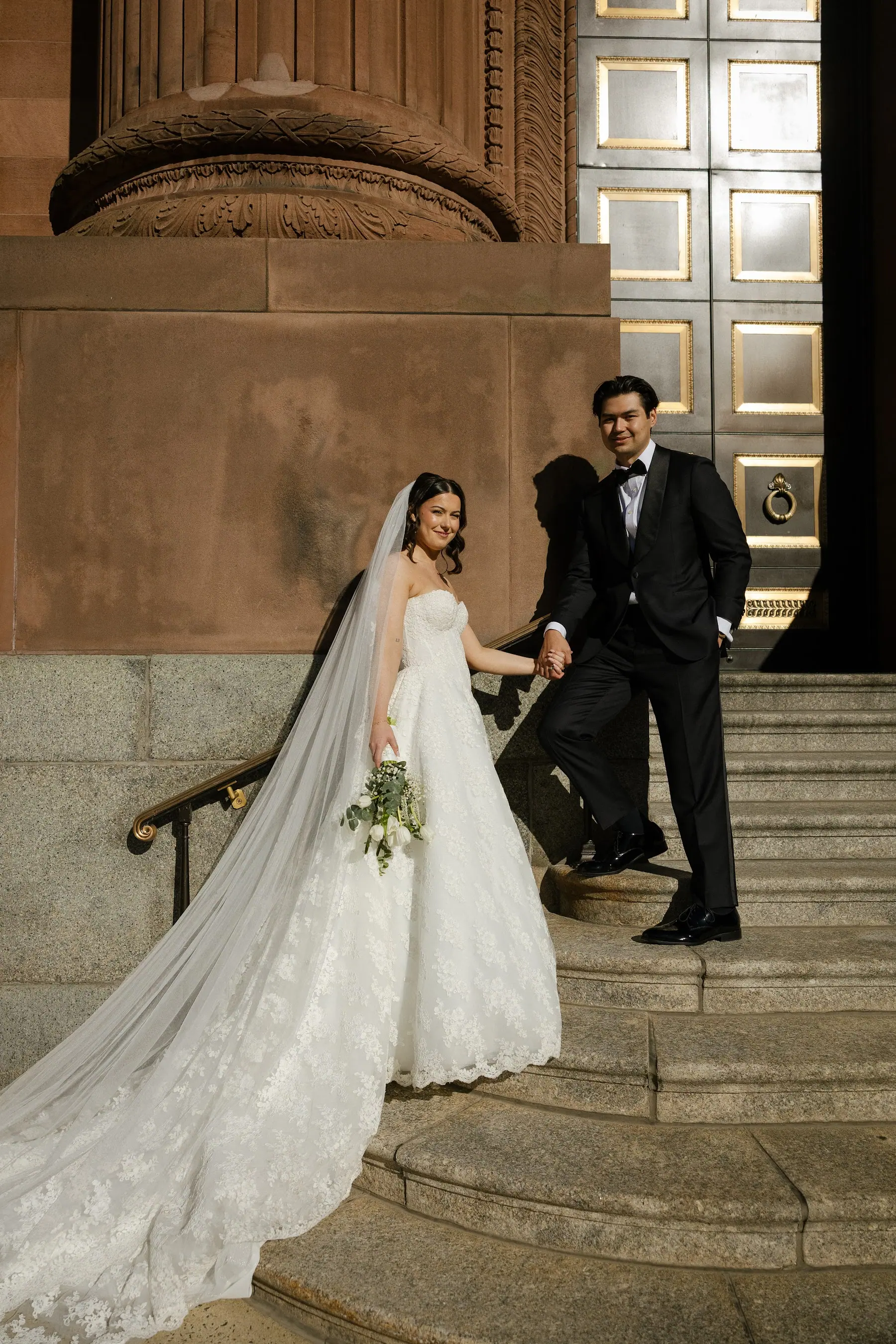 Bride and groom on the cathedral steps, cathedral veil trailing behind